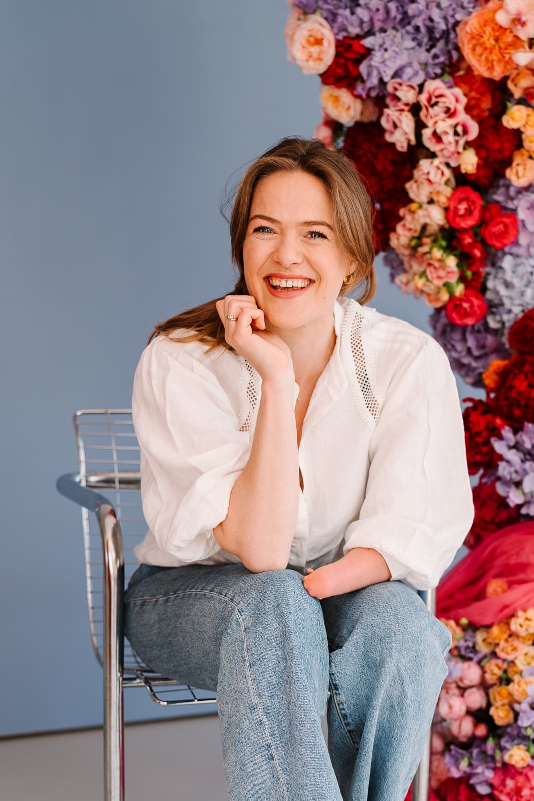 Marit Smit lacht, op een stoel voor een wand vol bloemen